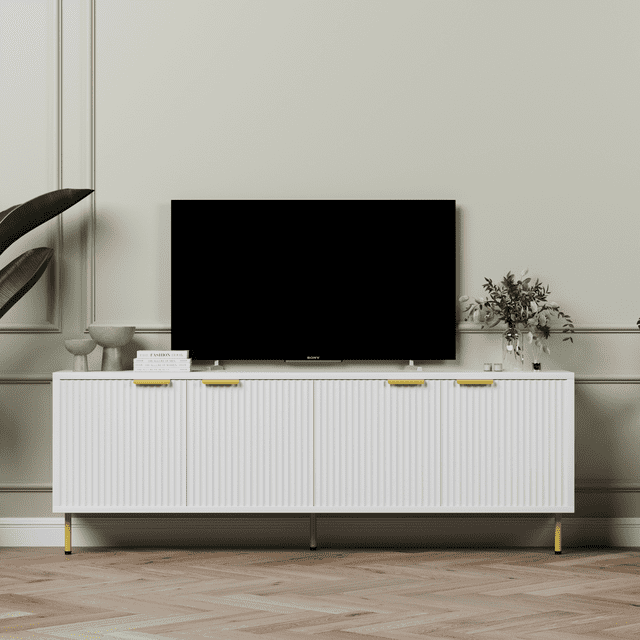 Aykah Luna Meuble Télé de 71 Pouces avec Rangement pour Télé jusqu'à 75 Pouces, Présentant un design Moderne avec une Finition Blanc Nette, des Portes d'Armoire Cannelées et des accents Métalliques Dorés. Ce Centre de Divertissement Comprend Quatre Armoires de Rangement à Fermeture en Douceur avec Tablettes Ajustables, Idéal pour Organiser l'Électronique, les consoles de Jeu et la Déco. Soutenu par des Pattes en Métal Doré, Ce Meuble Multimédia en Bois MDF durable Est Présenté dans un décor de Salon avec une Télé Montée et des Articles Décoratifs sur le Dessus.
