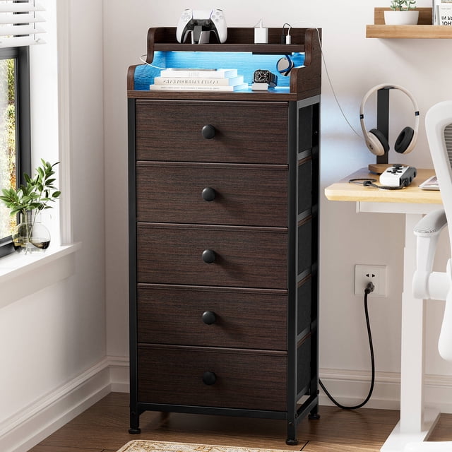 GUNAITO Commode Haute à DEL pour Chambre avec 5 Tiroirs, au design Mince et Léger en Brun. la Commode a un Cadre en Acier avec une Finition Noir Mat, un Dessus en Bois avec des Bords Surélevés et des Bacs de Rangement en Tissu. Elle Comprend Cinq Tiroirs Amovibles avec des Poignées à Tirage Fluide, des Pieds Ajustables pour la Stabilité et un Dispositif de Sécurité Anti-Basculement. la Commode Présente Aussi un Éclairage DEL Intégré avec 20 Couleurs et 5 Vitesses Réglables, Contrôlée via une Application mobile, et une station de Recharge Pratique avec 2 Prises, 2 ports USB et un Cordon D