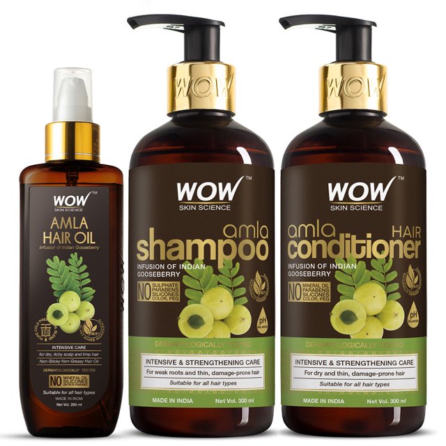 Wow Skin Science Amla Hair Care Kit featuring a 300ml bottle of Amla Hair Oil, a 300ml bottle of Amla Shampoo, and a 300ml bottle of Amla Conditioner. The set is designed for intensive care of weak roots and dry, brittle hair. Each product is infused with amla (Indian gooseberry) and other nourishing ingredients like cold-pressed oils, coconut oil, and sweet almond oil. The bottles have a sleek design with gold accents and clear labeling, emphasizing their sulfate-free and paraben-free formulas. Suitable for all hair types, this kit promotes scalp health, strengthens hair, and adds shine.