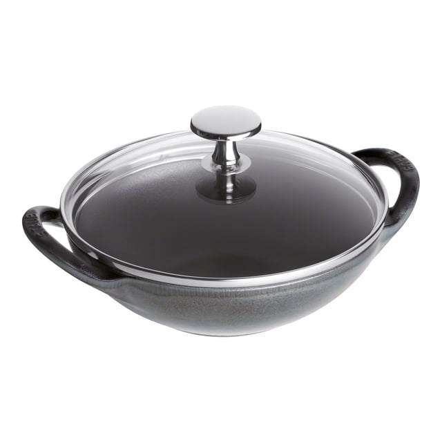 STAUB Specialities 16 cm / 6.5 inch Cast Iron Mini Wok in graphite-grey with a glass lid. The wok features a smooth enamel bottom suitable for all stovetops, including gas, electric, and induction. Made in France, it is oven safe up to 500°F and dishwasher safe. The black matte enamel interior enhances browning and braising, while the durable enamel exterior adds a stylish touch.
