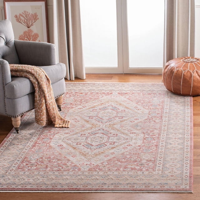 SAFAVIEH Kenitra Noelle Traditional Area Rug displayed in a bright living room, featuring a rectangular power-loomed accent rug with traditional ruby red, soft blue, beige, and ivory patterns framed by ornate borders. It rests on hardwood flooring beside a grey armchair with a knitted throw and a brown leather pouf. This durable area rug is also suitable for enhancing reading nooks or seating areas.