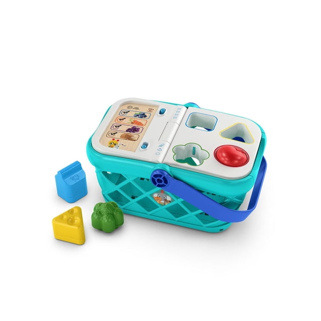 Baby Einstein - Magic Touch Shopping Basket™ pretend to shop toy in turquoise with blue handle and white lid featuring shape sorter cutouts for apple, broccoli, cheese, and milk shapes, plus a wooden panel with colorful food images and interactive buttons that play shopping sounds, music, and phrases in English, Spanish, French, and German.