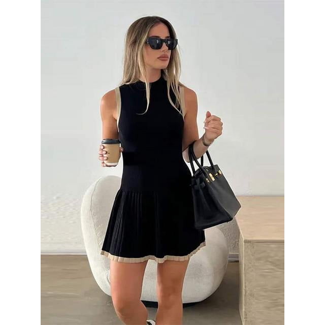 JUNWELL Robe Courte d'Été pour Femme Plissée Patchwork en Tricot de Golf 2024 avec un design Sans Manches avec un Col Rond Contrastant et un Ourlet Plissé. la Robe Noire Présente des accents Beiges le Long des Bords, Créant un Effet Patchwork Stylé. Convient aux occasions Décontractées Ou Sportives, la Coupe Ajustée Rehausse la silhouette. le Modèle Tient un Sac à Main Noir et Se Tient Debout dans un Cadre Intérieur Moderne.