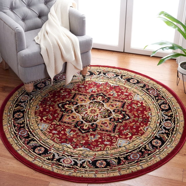 SAFAVIEH Lyndhurst Miranda Traditional Area Rug, round with a red base and intricate Persian floral and lattice patterns in black, beige, and blue, placed on hardwood flooring beside a gray armchair with a white knitted throw and near a green potted plant, ideal for busy home areas.