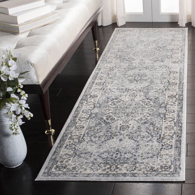SAFAVIEH Isabella Zander Floral Bordered Area Rug with traditional floral motifs in soft grey and blue hues, power-loomed synthetic medium cut pile, shown on dark hardwood floor beside a cream bench with brass-capped legs and a white vase with flowers, ideal for classic home accents.