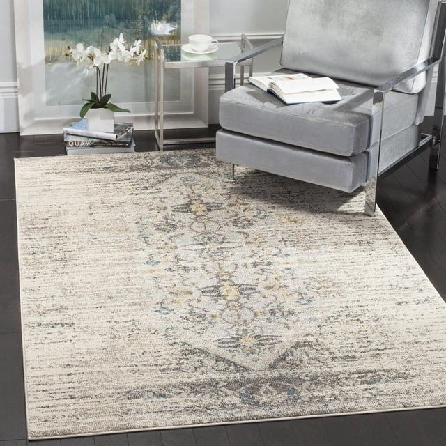 Safavieh Monaco Elsdon Abstract Area Rug featuring a muted beige and gray abstract pattern with blue and yellow accents, power-loomed polypropylene with mixed loop pile. It lies on dark hardwood flooring beneath a modern gray armchair with chrome arms, next to a glass side table with a white cup and saucer and a white orchid on books, suitable for adding Bohemian-chic style to home interiors.