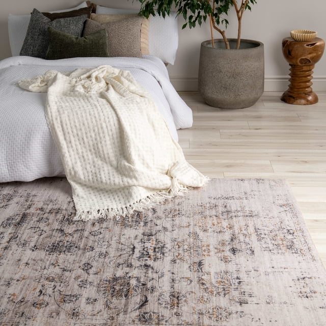 Rug Branch Emir Collection Tapis Traditionnel Oriental Usé Hydrofuge avec Motifs Floraux et Géométriques beige, Gris et Brun Atténués sur Plancher de Bois Clair dans une Chambre. le Tapis Complète une Literie Texturée Blanche avec un Jeté à Franges Crème et des Coussins Ton Terre. à Proximité Se Trouvent un Grand Pot en Béton Gris avec une Plante Verte et une table d'Appoint Sculpturale en Bois avec un Bol Décoratif, Rehaussant le style Minimaliste de la Pièce. Ce Tapis en polyester durable Convient aux Zones à Fort Passage et Est Facile à Entretenir.