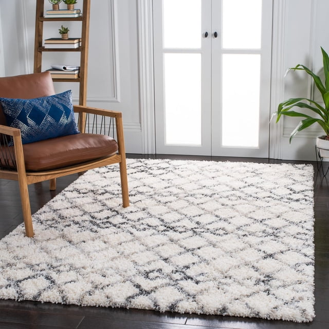Safavieh Fontana Aleta Geometric Distressed Plush Shag Area Rug with 2-inch plush pile in white and grey diamond pattern on dark hardwood floor, styled in a modern living room with a wooden armchair with brown leather cushions and blue geometric pillow, a wooden ladder shelf with plants and books, and a potted green plant near white French doors, ideal for adding comfort and texture to larger living spaces.