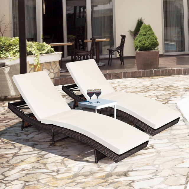 Costway Lot de 2 Chaises Longues Pliantes en Rotin pour Patio Chaise avec Coussins Blancs Réglables Exposés à l'Extérieur sur un Patio en Pierre. les Chaises Présentent un design en Rotin PE avec des Courbes Ergonomiques en Forme de « S », 5 positions de Dossier Réglables, et un design Pliable et compact pour un Rangement Facile. une Petite table Blanche avec Deux Lunettes Est Placée entre les Chaises.