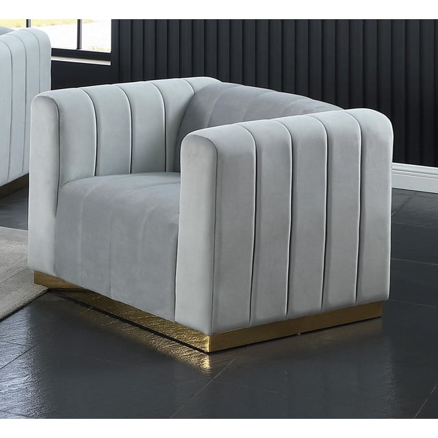 K-LIVING SHANNON Fauteuil en Velours Gris avec BASE Dorée d'Accent, Fauteuil d'Accent en Velours Gris Orienté vers l'Avant avec Canaux Verticaux Profonds Capitonnés sur les Accoudoirs et le Dossier, Soutenu par une BASE en Métal Doré, Convient aux Sièges de Salon et à la Déco d'Accent, Posé sur un Plancher de Carreaux Foncés contre un Mur à Panneaux Noirs.