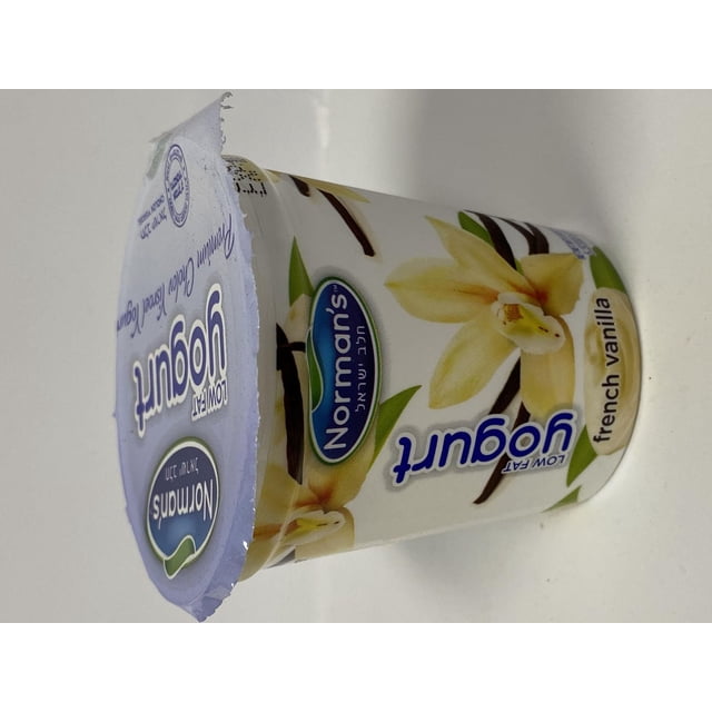 Norman's Vanilla Low Fat Yogurt in a white plastic cup decorated with vanilla flower and bean pod illustrations, sealed with a purple foil lid featuring the Norman's logo and product name, refrigerated French vanilla dairy yogurt ideal for a light snack or breakfast.