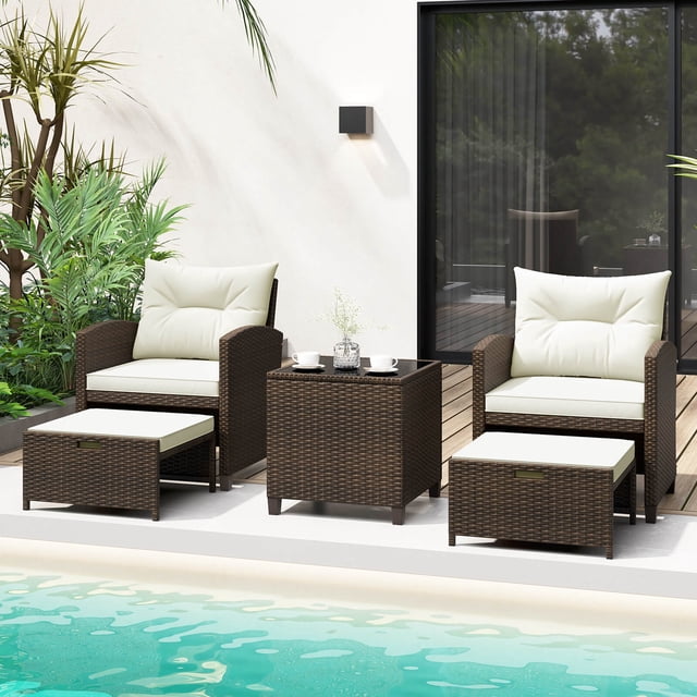 Costway 5 Piece Patio Rattan Furniture set featuring two mix brown PE rattan chairs with off-white cushions, two multifunctional ottomans, and a tempered glass coffee table. The chairs have ergonomic backrests and curved armrests for comfort, while the ottomans can serve as footrests, extra seats, or side tables. The coffee table includes a sturdy tempered glass top secured with suction cups. The set is displayed poolside with lush greenery and a modern patio backdrop.