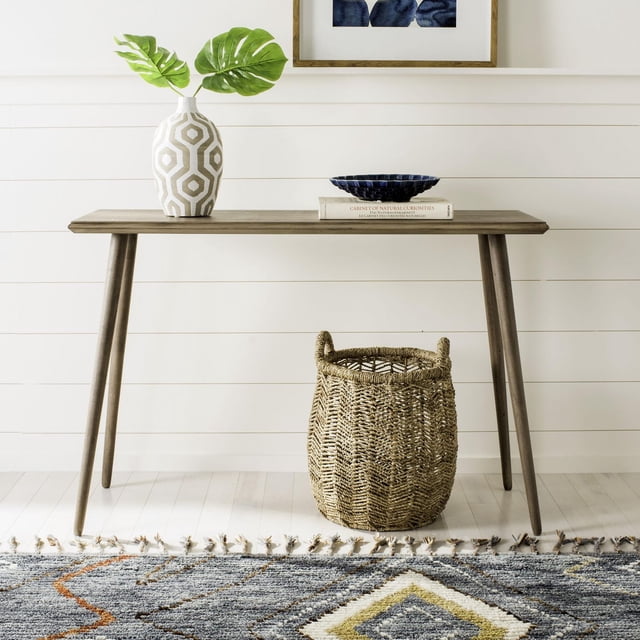 Safavieh Marshal Table Console Moderne Unie et Élégante, Fini Chocolat au Lait, avec Pattes Effilées, Style avec un vase Géométrique Blanc Tenant des Feuilles Vertes, un Bol Bleu sur un Livre et un Panier Tressé en Dessous, Posée contre un Mur shiplap Blanc et un Plancher de Bois Franc Clair avec un Tapis à Franges, Idéale pour accent et Présentation au Salon.