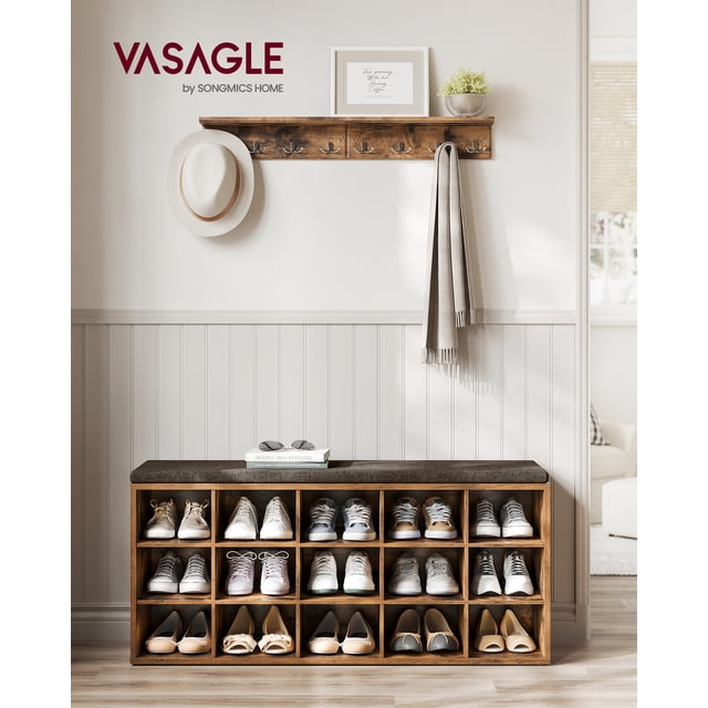 VASAGLE Banc à Chaussures, Banc de Rangement avec 15 Compartiments en Brun Rustique et Brun Châtaigne, Placé dans un Cadre d'Entrée. le Banc Présente un Coussin Rembourré et Amovible pour une Assise Confortable et une construction Robuste en Panneau de Particules Pouvant Supporter jusqu'à 440 lb. les Compartiments Sont Bien Organisés avec Diverses Paires de Chaussures, Mettant en Valeur Sa Capacité de Rangement. un Portemanteau Mural avec Crochets et des Articles Décoratifs comme un Chapeau, une Foulard et une Oeuvre Encadrée Complètent la Scène.
