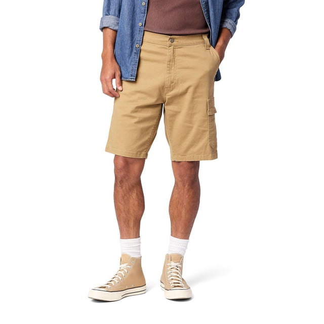 Levi Strauss Signature™ Men's Everyday Cargo Shorts in American Khaki with a relaxed fit, low waist, 10-inch inseam, and zip fly. Made from stretch Ultimate Flex Twill fabric (98% cotton, 2% elastane) featuring a side cargo pocket. Worn by a male model with a brown shirt, denim jacket, white socks, and beige high-top sneakers. Suitable for casual summer wear and outdoor activities.