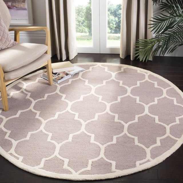 Safavieh Cambridge Kevin Geometric Area Rug, round with beige and cream geometric pattern, hand-tufted wool texture, on dark hardwood floor beside a light wood armchair and green plant near a window with beige curtains, suitable for home or office accent.