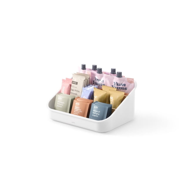 Umbra Bellwood Packet Organizer in white recycled plastic with three tiers and removable dividers, holding assorted colorful tea bags, snack packets, and small pouches, ideal for kitchen organization and pantry storage, shown in a front 3/4 view on a white background.