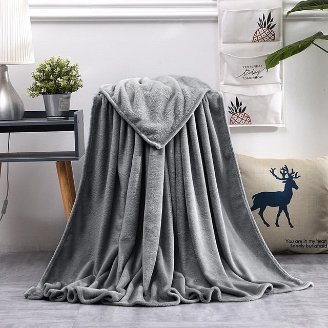 Super Soft Throw Blankets Super Soft Warm Solid Warm Micro Plush Fleece Blanket Throw Rug Sofa Bedding displayed in a cozy room. The flannel blanket, in a soft gray color, has a plush texture and is draped over a chair. It is machine washable, anti-static, and perfect for adding warmth and comfort to sofas or beds. A small table with a potted plant and decorative pillows completes the inviting scene.