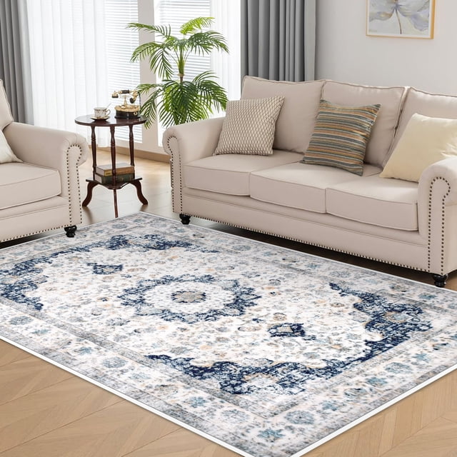 Meafeng 5'3" x 7'7" Area Rugs, Washable Rug for Bedroom Living Room, Home Decor Non-Slip Carpets(5x8), Blue centered front-facing view of a rectangular vintage-style polyester area rug in blue and grey with a muted floral medallion pattern and distressed shading; low-pile surface, stitched hem and flat non-slip backing edge visible, staged on a wooden floor in a neutral living room. Machine washable, suitable for bedroom or entryway use; often used to soften seating areas.