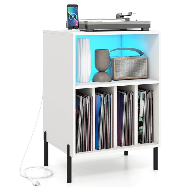 Costway Record Player Stand Turntable Stand with Vinyl Storage Holder & Shelf Table in white. Features a wide tabletop for turntable placement, an open shelf with integrated RGB LED lighting, and four divided compartments for vinyl record storage. Includes built-in charging station with 2 power outlets, 1 USB port, and 1 Type-C port, along with a cable management hole. Supported by sturdy metal legs with non-slip foot pads and anti-toppling kits for safety.