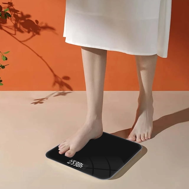 Meitianfacai Electronic Scale USB Charging Electronic Scale Body Scale Health Weighs Heavy Weight Scale shown in use. The black ABS scale features a high-precision digital display and compact dimensions of 26x26x2cm, ideal for bathroom accessories. A person is stepping on the scale in a minimalist setting with an orange background.