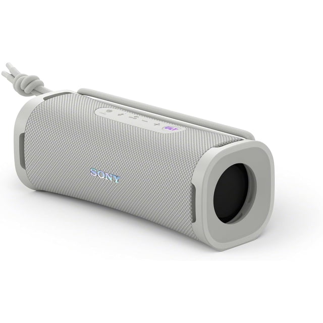 Sony ULT FIELD 1 Waterproof Bluetooth Wireless Speaker in off-white, shown in a close-up angled view. The portable speaker features a durable mesh exterior, multiway strap, and visible control buttons on the top panel. Designed for portability, it is water, dust, rust, and shockproof, making it ideal for outdoor use. Includes enhanced bass, stereo pairing capability, and up to 12 hours of battery life. Open box condition with a USB cable included.