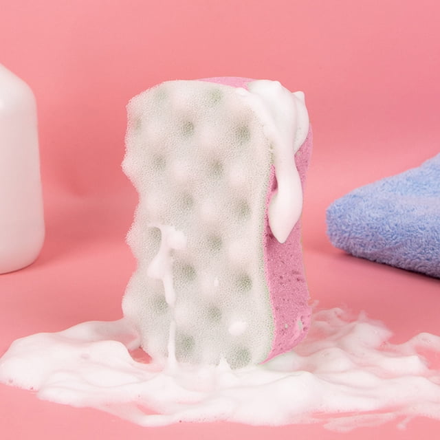 TopLLC Wave Bath Sponge, a dual-sided bath accessory made of pink and white polyester, designed for efficient cleaning and exfoliation. The sponge is shown producing abundant foam, ideal for sensitive skin and removing dead keratin. Set against a pink background with a blue towel and white bottle nearby.