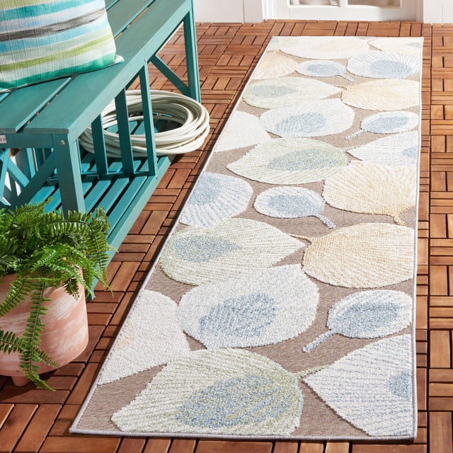 SAFAVIEH Sarasota Nash Floral Indoor/Outdoor Area Rug with a beige background and large textured leaf patterns in soft blue, cream, and green tones, placed on a wooden deck beside a teal bench with a striped cushion and a potted fern, designed for weather-resistant durability and suitable for both indoor and outdoor use.