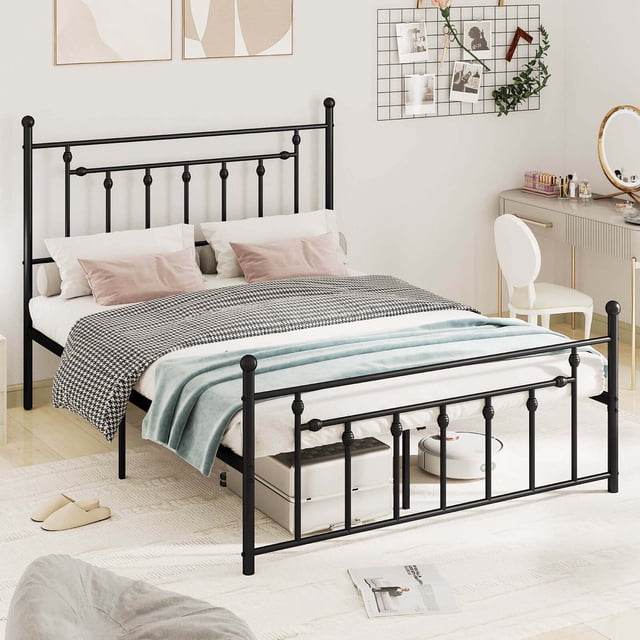 Costway Queen Size Metal Bed Frame with Headboard Under-bed Storage Mattress Foundation displayed in a modern bedroom. The heavy-duty black metal frame features an industrial-style headboard and footboard with decorative vertical bars. It includes 9 supportive legs and a metal slat system, eliminating the need for a box spring. The bed offers 12.5 inches of clearance underneath for storage, with visible items like luggage and a sweeping robot stored below. The mattress is styled with a houndstooth-patterned blanket and pastel pillows, complementing the room's neutral decor.
