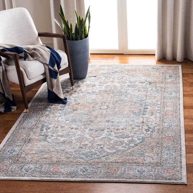 SAFAVIEH Oregon Avalon Tapis Traditionnel Usé Présentant un grand Médaillon central et une Bordure Florale dans des Tons Bleu, beige et Ivoire Atténués avec une Patine antique, Posé sur un Plancher de Bois Franc dans une Pièce Lumineuse. le Tapis en Fil Synthétique Tissé Mécaniquement Est Montré sous un Fauteuil beige avec des Accoudoirs en Bois et un Jeté Bleu et beige, à Côté d'Un grand Pot Gris avec une Plante Serpent. Idéal pour Ajouter un accent Traditionnel durable et vintage aux Espaces de Vie.