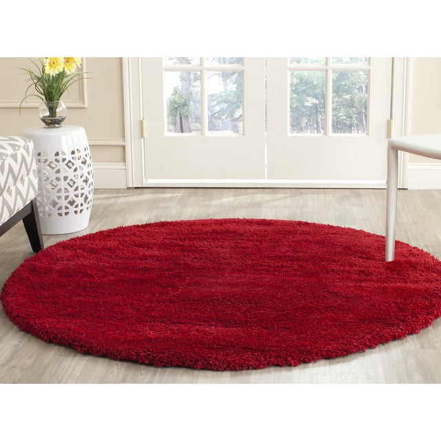 Safavieh Milan Harlow Solid Shag Area Rug in a round vibrant red design with plush synthetic yarns, placed on light wood flooring in a bright room with white French doors, a patterned sofa, a white ceramic side table with cutout details, and a vase with yellow flowers, suitable for adding warmth and texture to contemporary home décor.