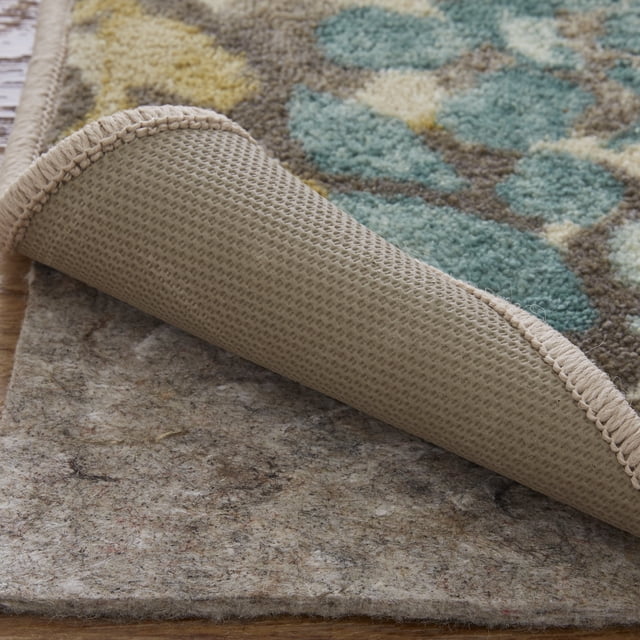 Mohawk Home Premium Dual Surface Rug Pad, 9' X 12', Grey, displayed under a patterned area rug with a corner lifted to show the textured grey pad. Ideal for non-slip grip and added cushioning on hard floors or carpets.