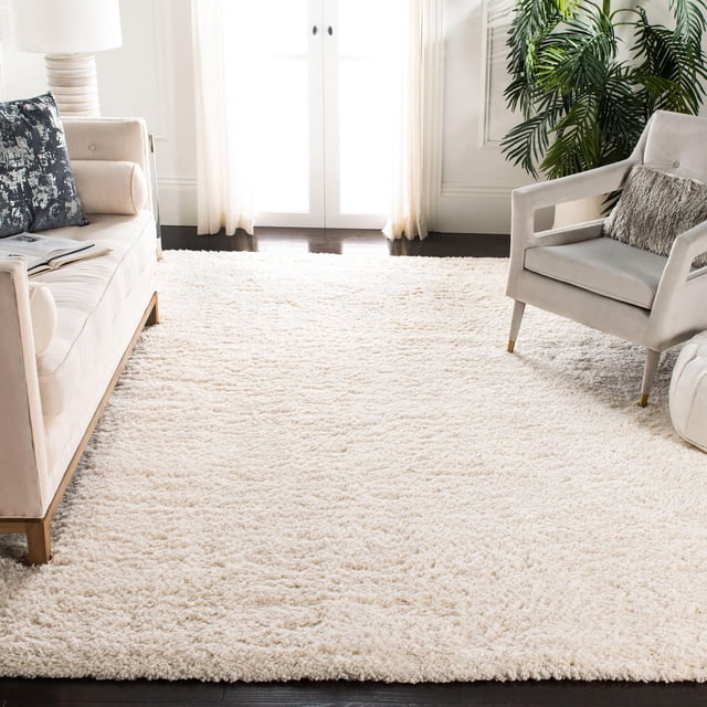 SAFAVIEH Fontana Jamie Tapis Shag Moelleux Uni avec texture Shag Peluche de 2 Pouces en Blanc Cassé Uni, Posé sur un Plancher de Bois Franc Foncé dans un Salon Lumineux entre un sofa beige et un Fauteuil Gris, Accentué de Rideaux Transparents et d'Une Grande Plante Verte, Convient pour Rehausser la Déco de Tapis d'Accent Moderne.
