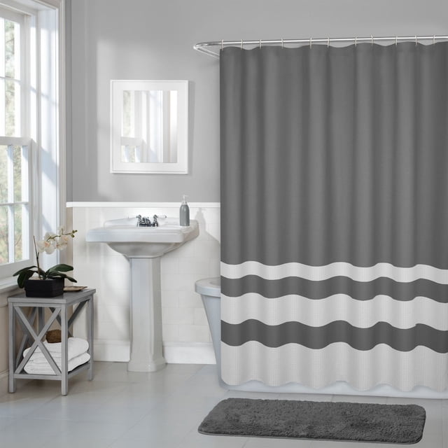 Hometrends Textured Waffle Stripe Fabric Shower Curtain in grey with two-toned waffle stripe design, hanging on a curved shower rod in a bathroom with white pedestal sink, mirror, grey bath mat, and wooden side table with towels. The fabric curtain is machine washable and fits standard tubs, suitable for enhancing bathroom decor with a textured fabric look.