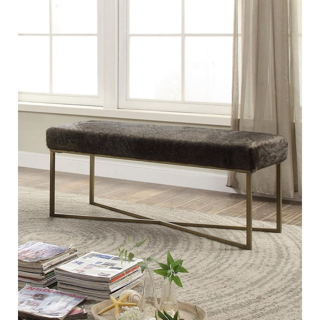 K ELITE Filia Fur Bench Dark Grey with a rectangular dark grey faux fur upholstered seat on a gold metal frame with crossed legs, placed on a circular textured rug near large windows with sheer curtains, ideal for entryway seating or as a storage bench.