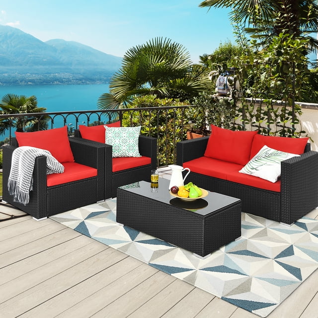 Patiojoy 4PCS Patio Rattan Wicker Conversation Furniture Set, ideal for outdoor patio use, includes a black rattan loveseat, two single sofas, and a coffee table with tempered glass top. Features red cushions with ergonomic backrests and armrests, placed on a wooden deck overlooking a scenic lake and surrounded by lush greenery.