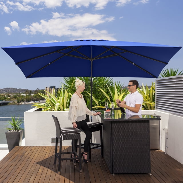 Costway Parasol Déporté de Patio 10 Pieds X 13 Pieds Bleu Marine avec Cadre en Aluminium, Doté d'Un Grand Auvent Offrant 130 Pi2 d'Ombre. Ce Parasol de Patio Comprend une Fonction de rotation à 360°, des Réglages d'Inclinaison à 4 Niveaux et un Système à Manivelle pour un Fonctionnement Fluide. Positionné sur une Terrasse en Bois avec une table de bar et des Chaises, Entouré de Verdure et une Vue sur le Bord de l'Eau.