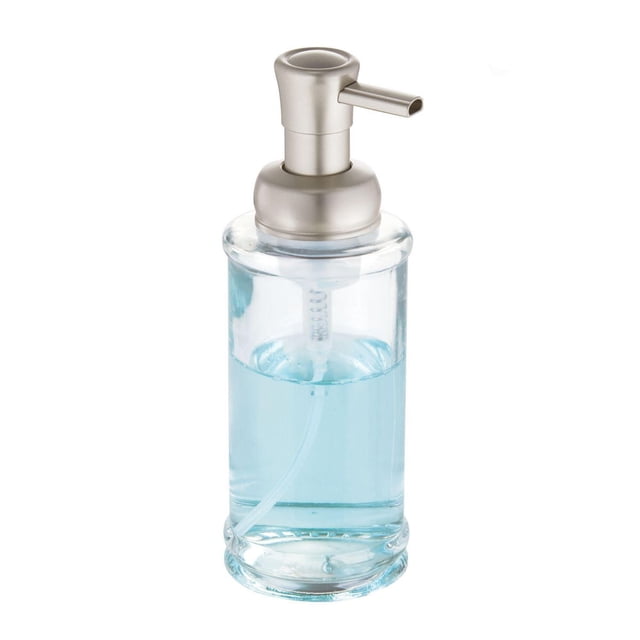 iDesign Hamilton Clear Glass Foaming Soap Pump with a clear glass body holding blue liquid soap and a brushed plastic pump head, measuring 3 by 3 by 8.3 inches, designed for bathroom or kitchen countertops with a wide refill opening and stable base to prevent slipping, also suitable for dispensing hand sanitizer or lotion.
