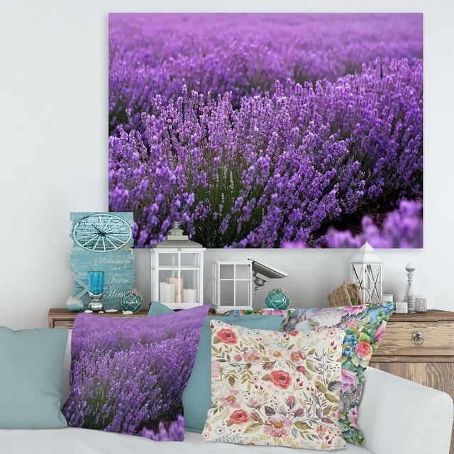 Designart Blooming Purple Lavender Field Canvas Wall Art depicting a close-up of dense purple lavender flowers printed on premium cotton canvas with fade-resistant ink and gallery-wrapped edges, displayed above a rustic wooden console with floral cushions and decorative lanterns, arriving ready to hang and ideal for enhancing farmhouse-style home décor.