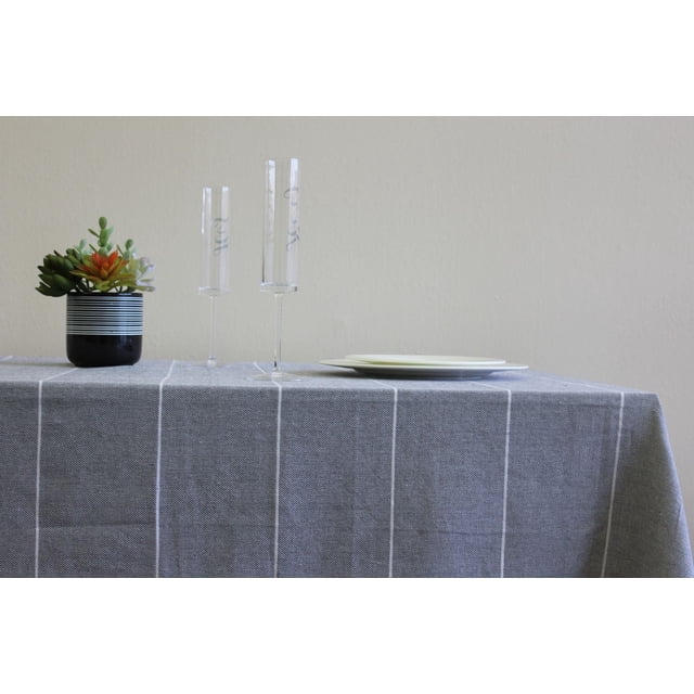 Fabstyles Fouta 100% Cotton Stripe Table Cloth in grey with white vertical stripes draped over a dining table, styled with two clear champagne flutes, stacked white plates, and a small black pot holding green and orange succulents, suitable for indoor dining and casual entertaining.