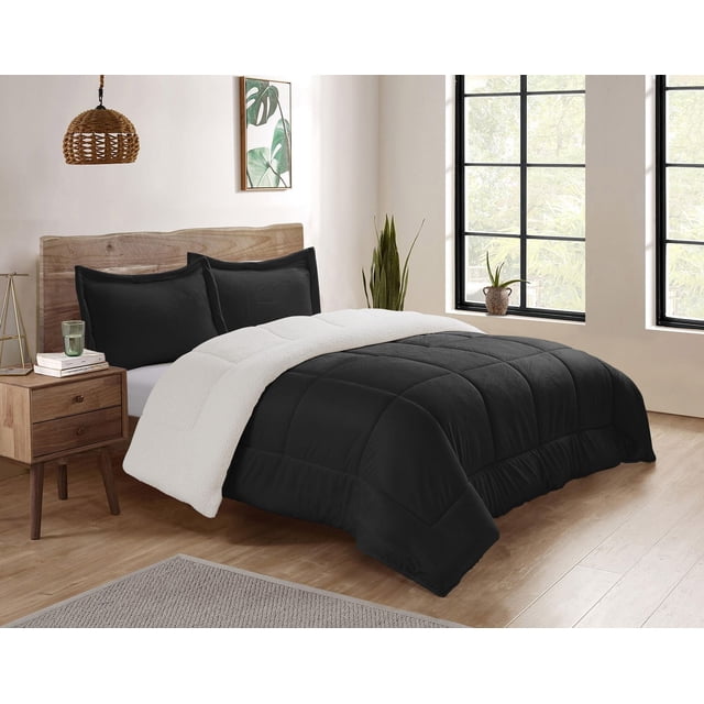 Reversible Mink & Berber Plush Sherpa Comforter Set on a bed with a natural wood headboard in a bright room. The comforter shows a black plush side and a white Sherpa fleece reverse, paired with matching black pillow shams. The setting includes a wooden nightstand with books and a glass, a woven pendant light, botanical wall art, and large black-framed windows overlooking greenery. This set is often used to enhance bedroom warmth and softness.