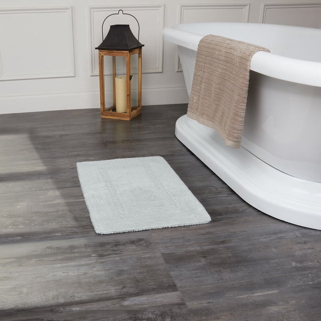 Fabstyles Basix Tapis de Bain en Coton Réversible Doux et Absorbant Gris Pâle sur Plancher de Bois Foncé à Côté d'Une Baignoire Autoportante Blanche avec une Serviette beige Drapée sur le Bord et une Lanterne en Bois avec Bougie Près d'Un Mur à Panneaux Blancs, Idéal pour la Douche, la Baignoire Ou l'Évier.