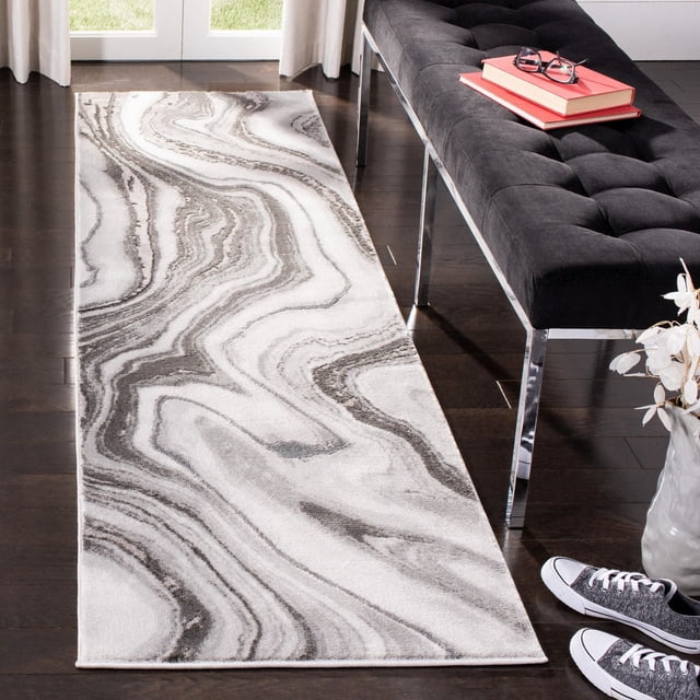 SAFAVIEH Craft Angjelko Abstract Area Rug, a durable runner with swirling grey and white abstract patterns and subtle etched pile texture, placed on dark hardwood flooring beside a black tufted bench with chrome legs and books, ideal for contemporary hallways or entryways.