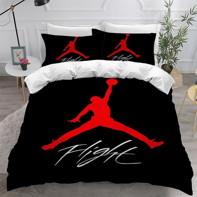 Jordan-1# Jordan Digital Printing Three-piece 3d Trapeze Logo Quilt Cover Air Pillowcase set featuring a bold red silhouette of a basketball player in mid-air against a black background with the word 'Flight' in white script. The bedding set includes a quilt cover and two matching pillowcases, made from chemical fiber with a polished finish and digital printing. Available in sizes 180x210 cm, 200x230 cm, and 220x240 cm. Displayed in a modern bedroom setting with white walls, a side table, and decorative plants.