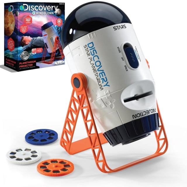 Discovery Projecteur de Jouets Spatiaux et de Planétarium en Forme de Vaisseau Spatial Cylindrique Blanc avec Dessus en Dôme Noir et Marque Discovery Bleue, Monté sur un Support orange Ajustable, Montré avec Trois Rouleaux Coulissants photo Colorés en Bleu, Blanc et orange, aux Côté de Sa Boîte d'Emballage à Thème Spatial.