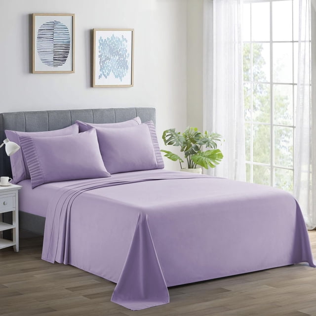 Marina Decoration Ultra Soft Silky Deep Pocket Solid Rayon from Bamboo Bedding All Season Sheet Set in purple on a made bed with a grey upholstered headboard. The set includes a deep pocket fitted sheet, flat sheet, and pleated pillowcases. The fabric is soft, wrinkle-resistant, breathable, and durable. The bed is in a bright room with wood flooring, a white nightstand holding a lamp and cup, two framed blue abstract artworks on the wall, and a green potted plant by a large window with sheer white curtains. This sheet set is also suitable for year-round comfort and easy machine care.