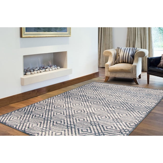 ECARPET Area Rug for Living Room, Geometric Indoor Carpet Ember Collection with a rectangular rug featuring a muted grey and beige diamond geometric pattern on hardwood floor, placed in a living room with a beige armchair, black leather chair, and modern recessed fireplace with decorative stones, often used to enhance indoor decor with contemporary style and warmth.