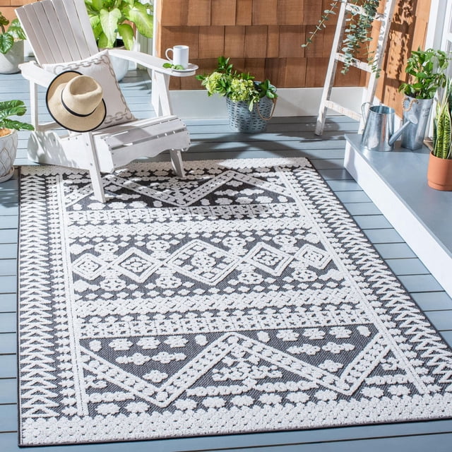 SAFAVIEH Cabana Arielle Tapis Géométrique Intérieur/extérieur avec Losanges Noir et Blanc et Motifs Floraux sur une Terrasse en Bois Grise, à Côté d'Une Chaise Adirondack Blanche avec un Coussin beige et un Chapeau de Paille, Entouré de Plantes en Pot et d'Arrosoirs en Métal, Convient aux Zones Occupées Intérieures Ou Extérieures.