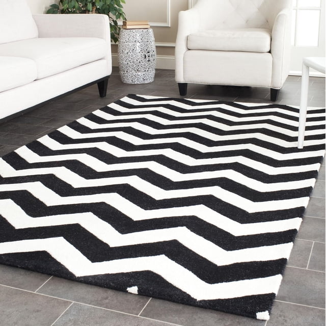 Safavieh Chatham Jake Tapis à Rayures Zigzag avec Rayures Zigzag Noires et Blanches et un Velours de Laine Moelleux de Hauteur Moyenne, Posé sur un Plancher de Carreaux Gris entre un sofa et un Fauteuil Blancs dans un Salon Moderne avec une table d'Appoint Décorative en Céramique et une Plante Verte, Souvent Utilisé pour Rehausser des Espaces d'Accent Contemporains.