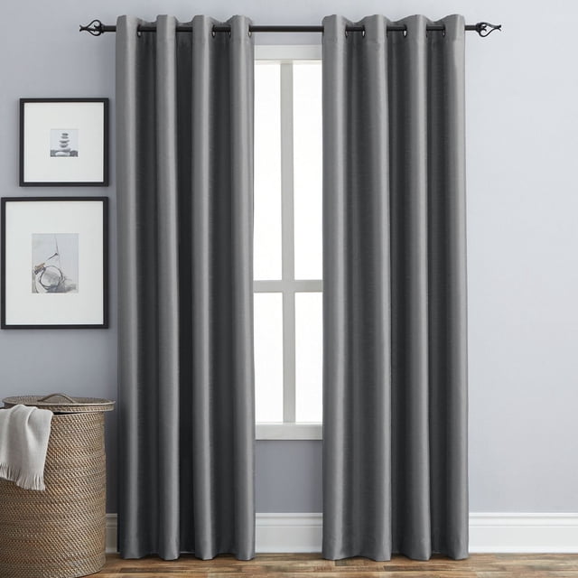 Hometrends Faux Silk Grommet Room Darkening Window Curtains Panel in dark grey with thermal lining that blocks 99% of light, hanging on a black metal rod with grommet top, displayed in a room with light grey walls, framed art, and a woven basket with a white throw, ideal for reducing drafts and noise.